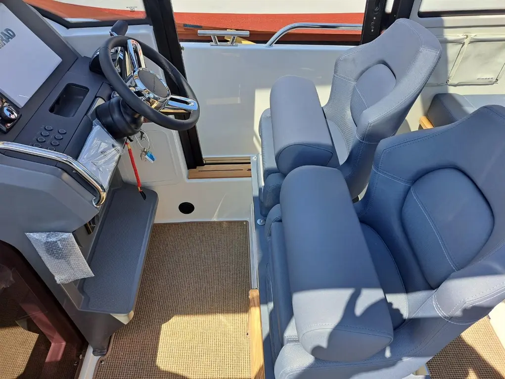 Boat interior showing a steering wheel, controls, and two comfortable blue seats on a textured floor mat.